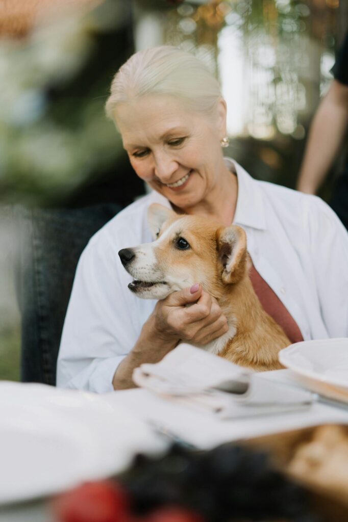 Elderly woman smiling and holding her corgi pet, radiating joy.